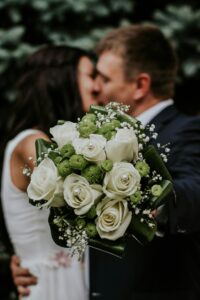 Pareja de novios abrazados con ramo de rosas blancas y flores verdes, símbolo de amor y frescura en una boda elegante